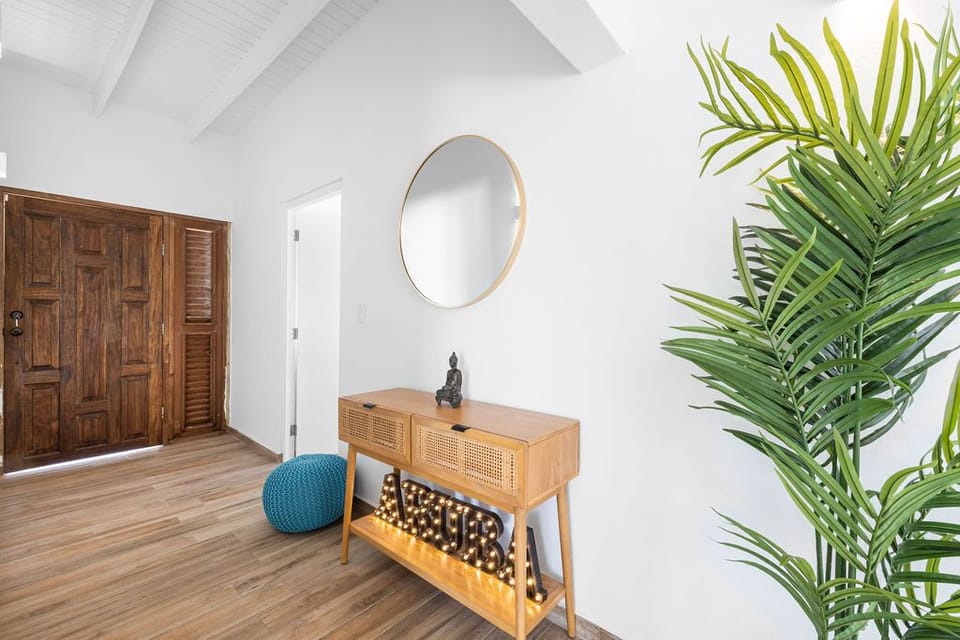 A beautiful round wall mirror, wooden floor and furniture and indoor plant in the entryway corridor.