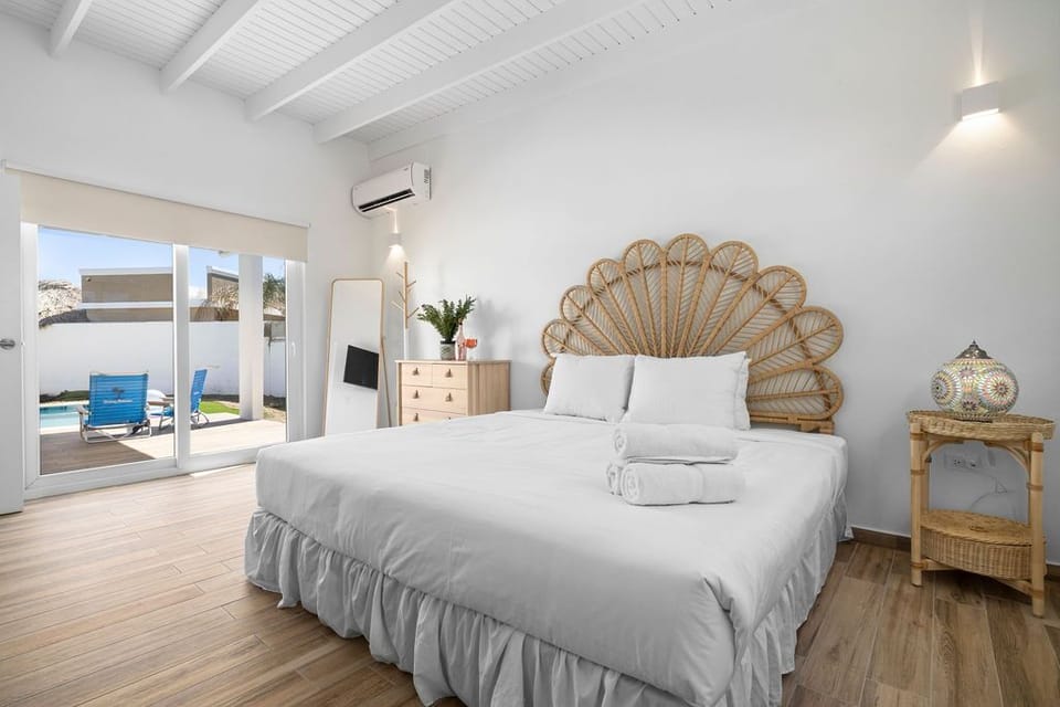 This bedroom features a king-size bed and en suite bathroom. It has air-condition, wooden craft furniture, and indoor plant.