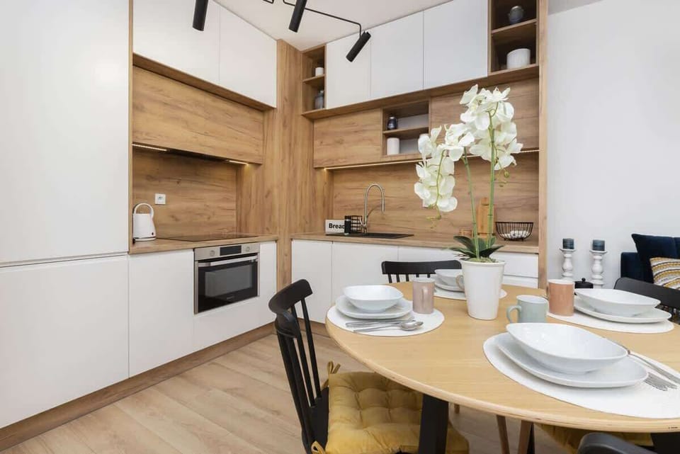 A modern kitchen with light wooden cabinetry and a small dining area. The kitchen is well-lit with contemporary design elements.