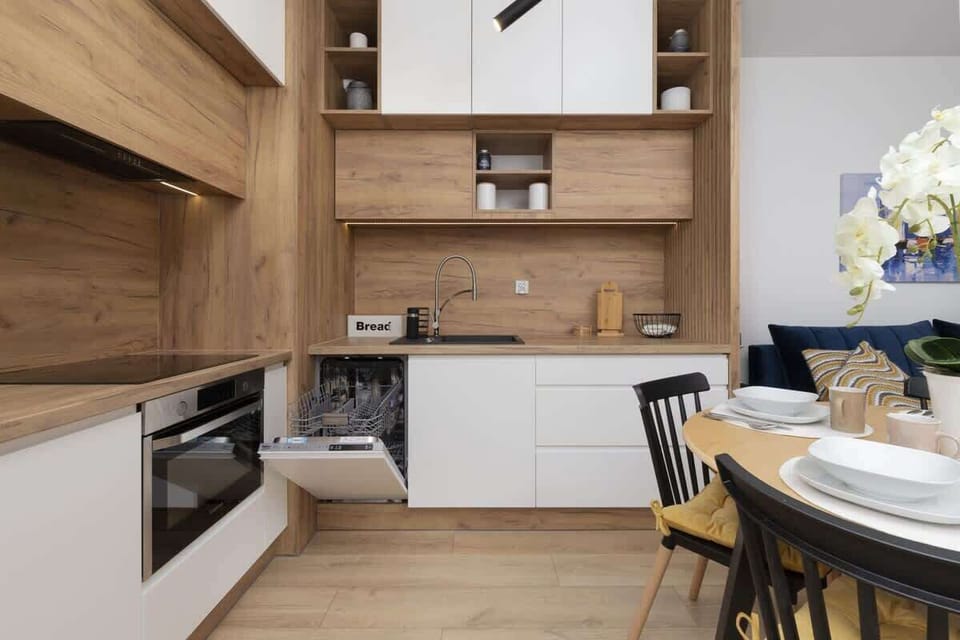 A wide view of the kitchen, showcasing wooden cabinets, a dining table, and built-in appliances. The space is stylish yet functional.