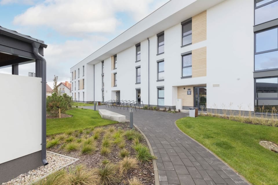 A view of the exterior of a modern apartment building with a clean, minimalist design and a landscaped walkway.
