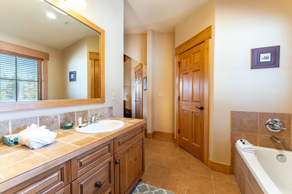 Unwind in your spacious bathroom featuring warm wood cabinetry, dual sinks, and a relaxing soaking tub perfect for evening retreats.