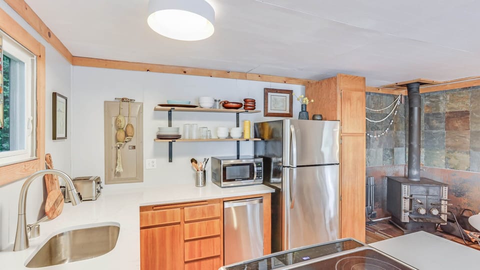 Stainless steel appliances, counter space, open shelving, & wood stove.