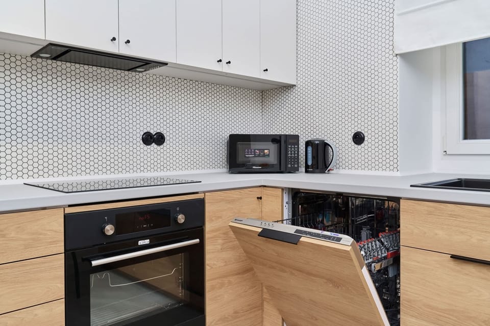 A modern kitchen with a functional layout, including built-in appliances, a patterned backsplash, and light wood finishes.