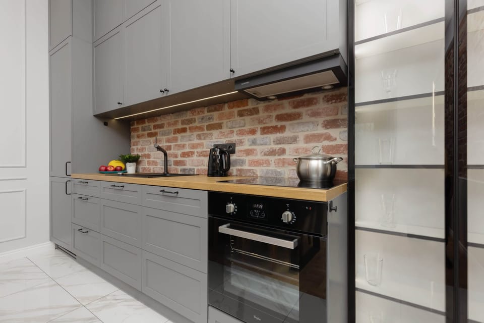 A sleek kitchen featuring gray cabinetry, built-in appliances, and a brick backsplash.