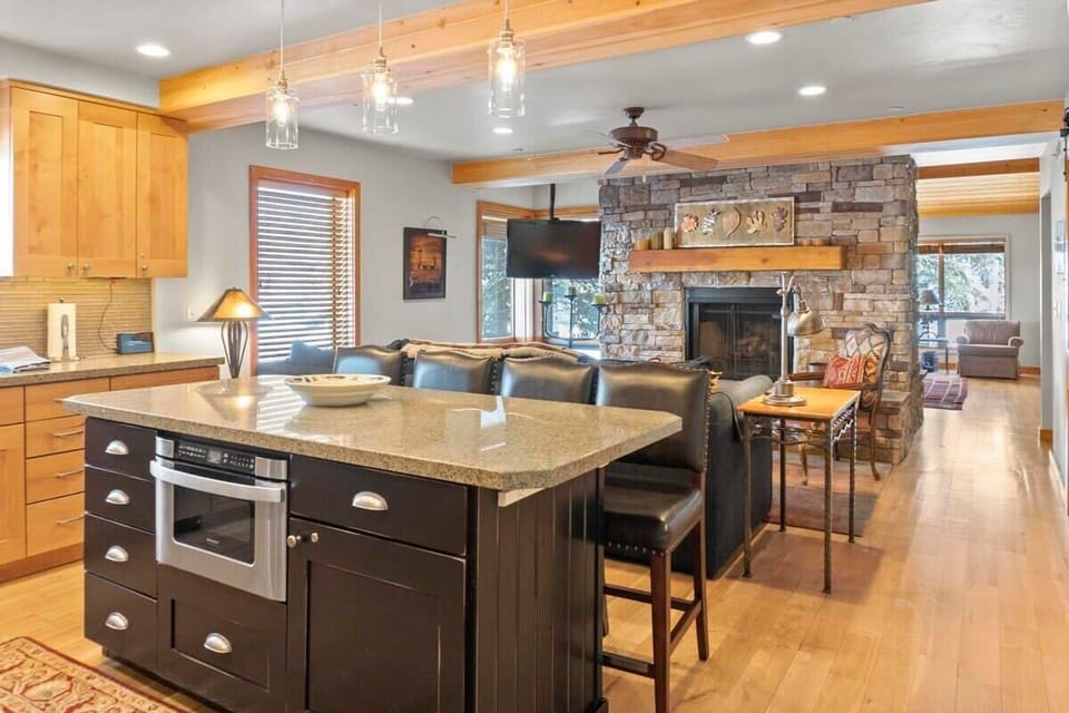The spacious open kitchen and living room are filled with charming features such as exposed wood ceiling beams, a beautiful stone hearth double-sided fireplace, and modern light fixtures.