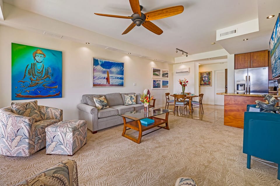 Lounge in this vibrant, art-filled living room featuring tropical furnishings, ceiling fan, and smart layout—steps from beaches and golf courses.