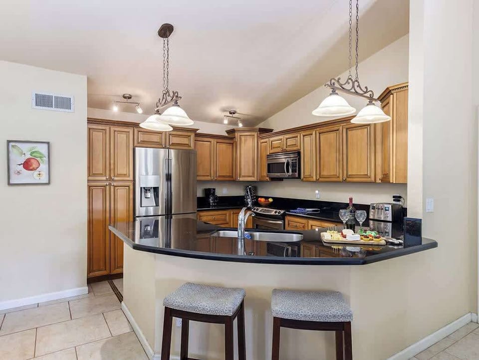 Fully equipped kitchen with stainless steel appliances, breakfast bar seating, and dining table with seating for 4 guests.