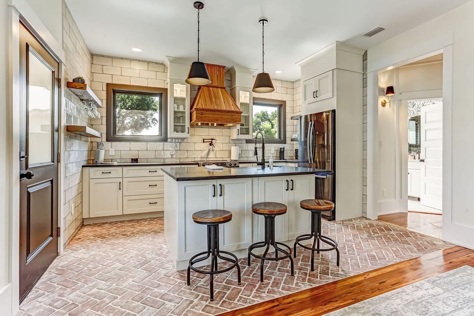 -Experience rustic modern charm with brick floors, white tile walls, and wood accents
- Kitchen island with barstools and pendant lighting perfect for casual dining
- Door and windows bring natural light and seamless access to the deck