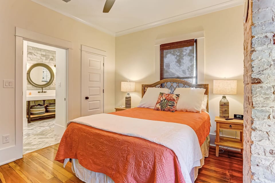 - Rest comfortably in this cozy bedroom featuring warm wood floors and an orange quilt
- En suite bathroom access and dual nightstands create a relaxing and functional setup
- Textured brick detail and soft lighting add unique character