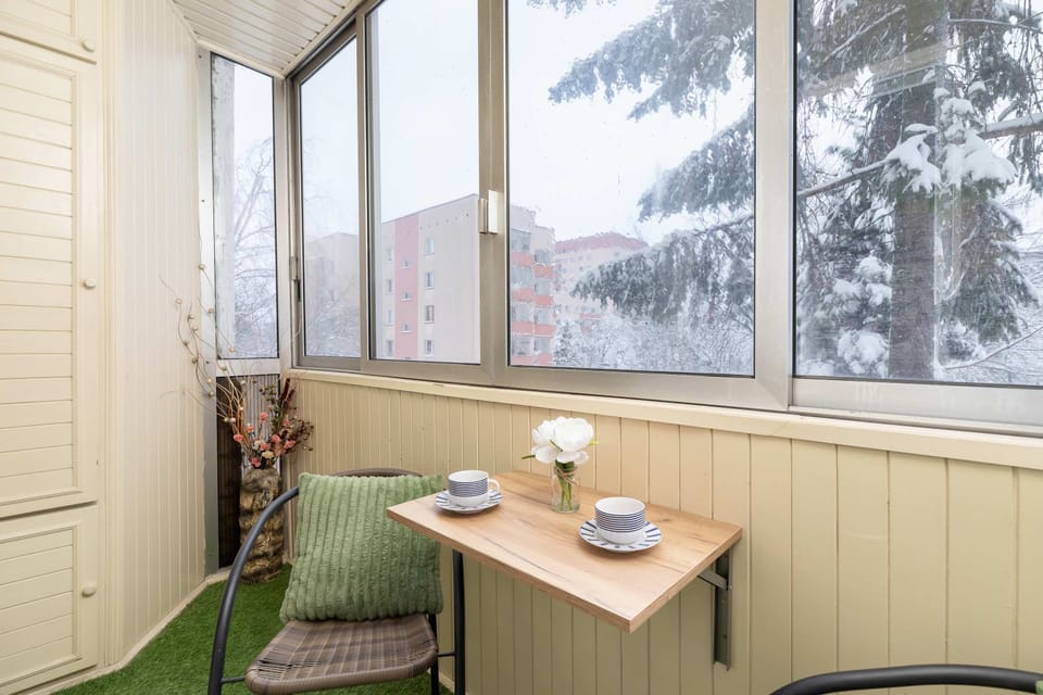 An enclosed balcony setup with a small table, chairs, and green accents.
