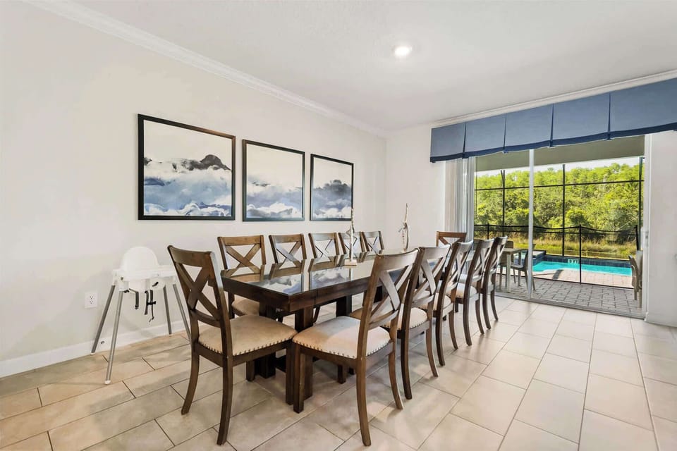 Spacious private dining room with seating for 12, framed artwork, and sliding glass doors overlooking the pool and lush wooded surroundings.