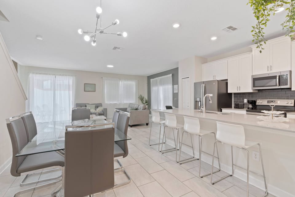 Experience a chic and functional kitchen and dining space featuring a stylish island, modern bar stools, and a glass dining table.