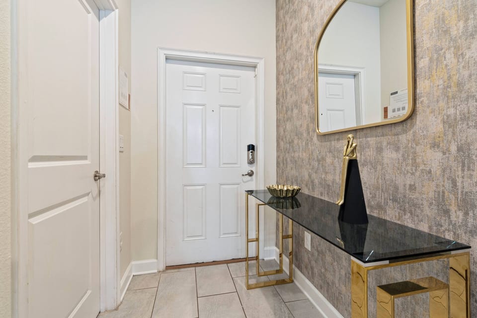 Enter a stylish entryway that welcomes you with a sleek black console table and a chic gold-framed mirror. The textured wallpaper and abundant natural light create a warm and inviting atmosphere for your stay.