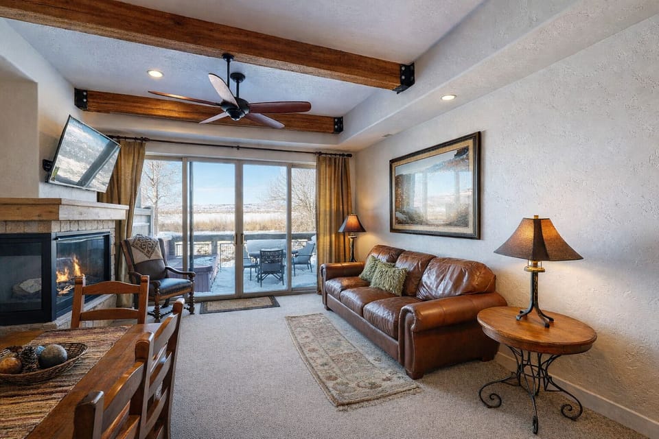 Relax in this mountain-modern sanctuary featuring a plush leather sofa, rustic beam ceilings, and warm lighting. Expansive glass doors offer a seamless connection to your private, scenic balcony.