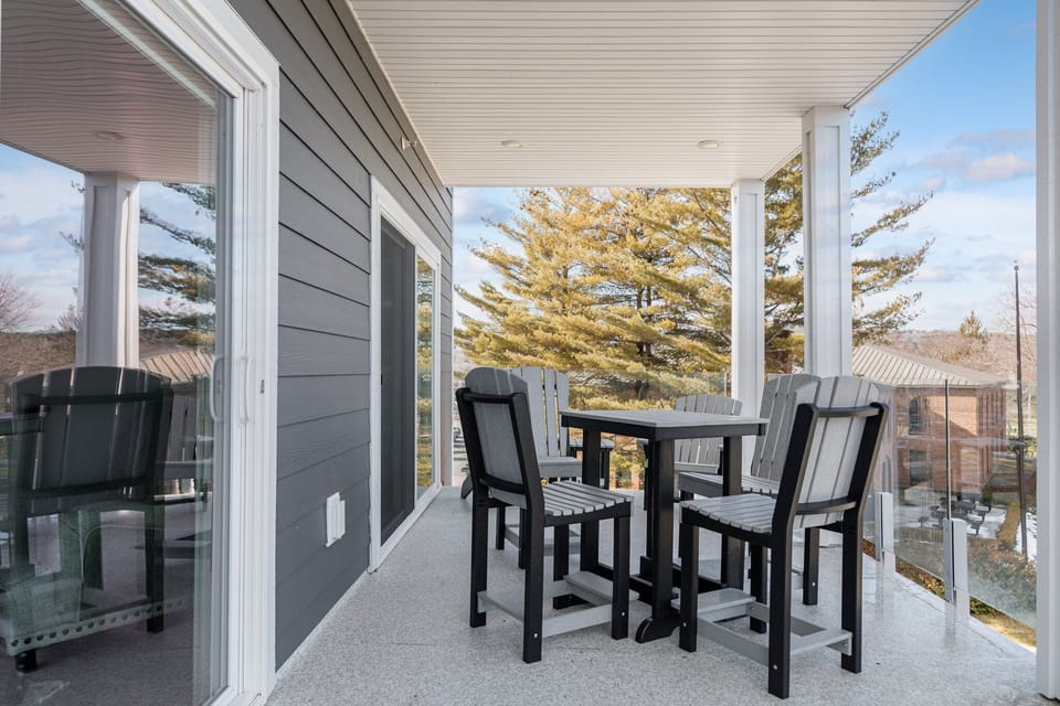 Covered balcony with a high outdoor dining table and chairs beside a glass railing.