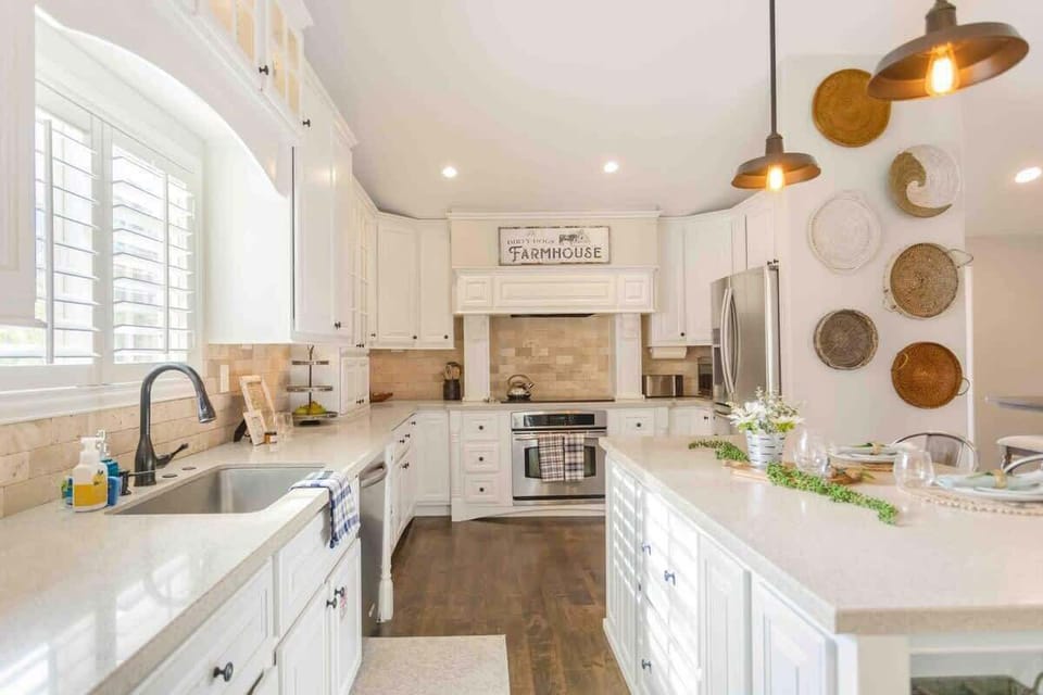 a farmhouse style kitchen with white cabinets, a large center island with a granite countertop, and open shelves displaying rustic dishes and accessories.