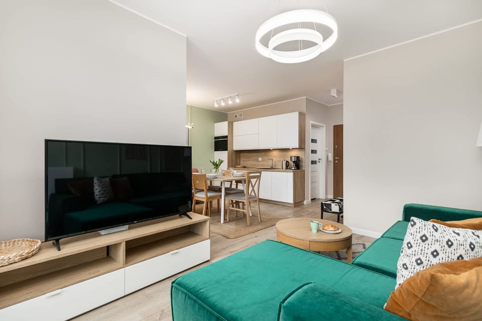 A view of the living room with a mounted TV, green accents, and a stylish chandelier.
