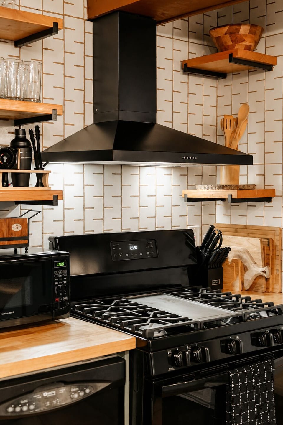 Prep meals on the black gas range and the nearby floating wood shelves keep your glassware and cooking essentials within reach for easy dinner service.