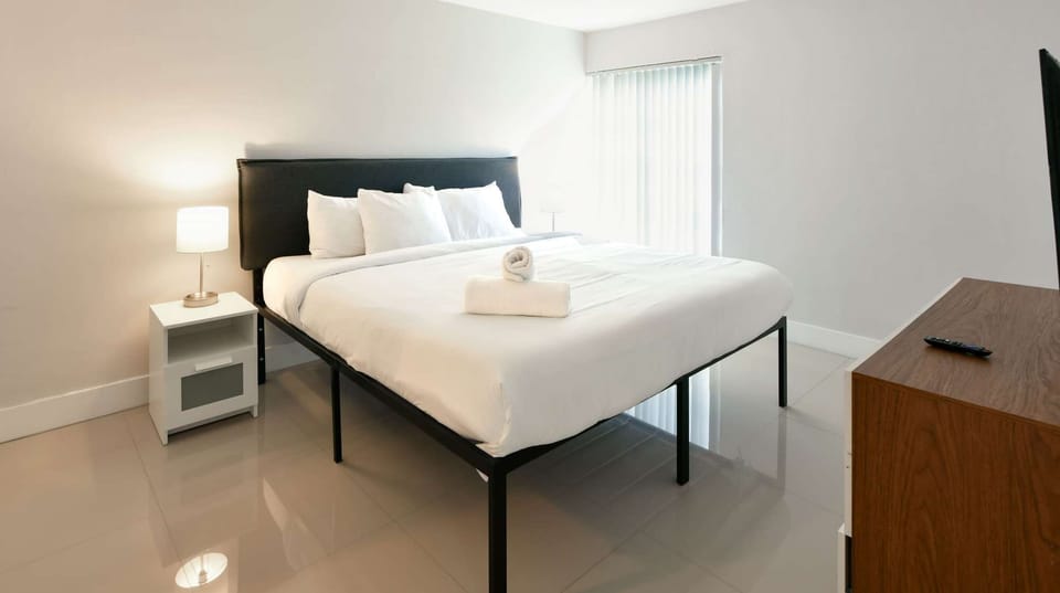 Bright king bedroom with side table, lamp, dresser, and TV