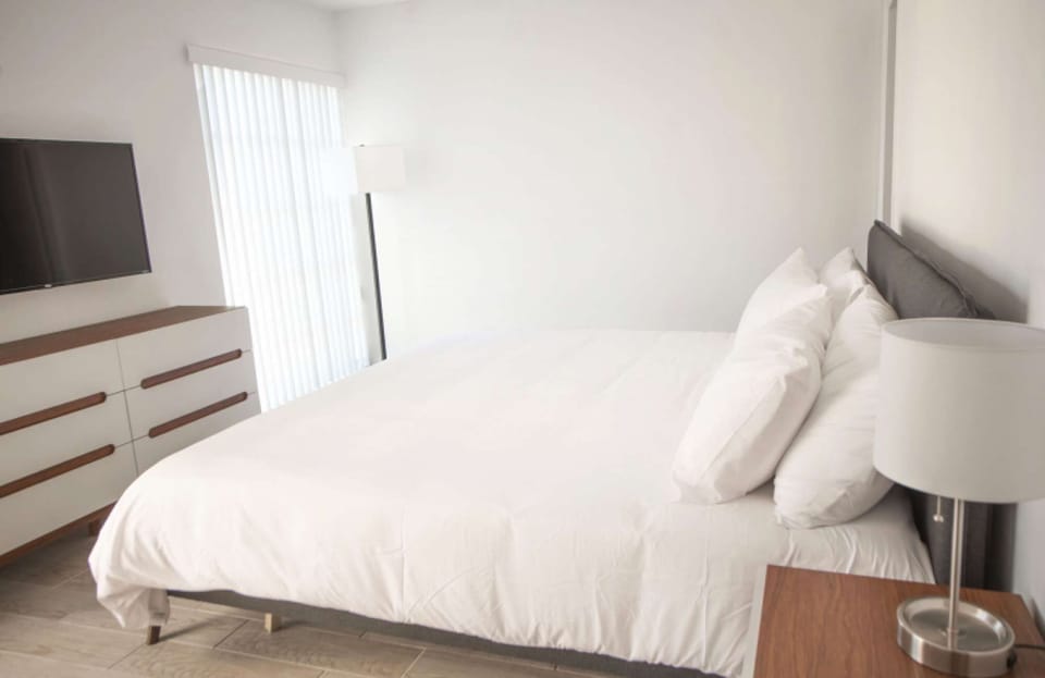 Bright king bedroom with dresser, TV, lamp, and window blinds