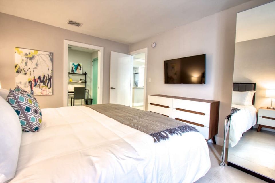 Bright bedroom with wall TV, dresser, mirror, and open doors