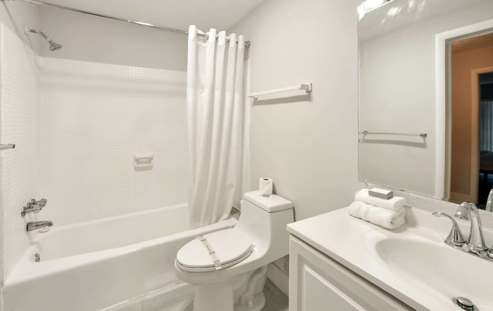 Bright bathroom with tub shower, sink, mirror, and soft towels