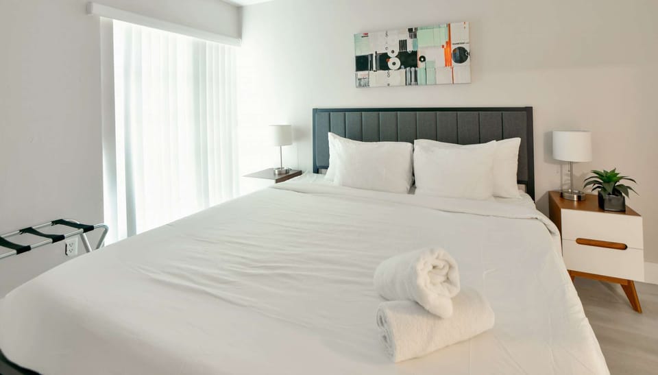 Bright king bedroom with side lamps, wall art, and window blinds