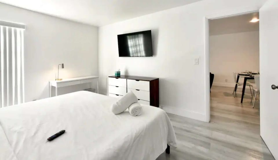Bright bedroom with TV, dresser, desk, and open doorway