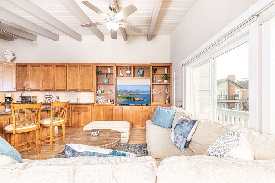 The living area includes a large L-shaped couch, streaming TV, and sliding door to the front balcony.
                