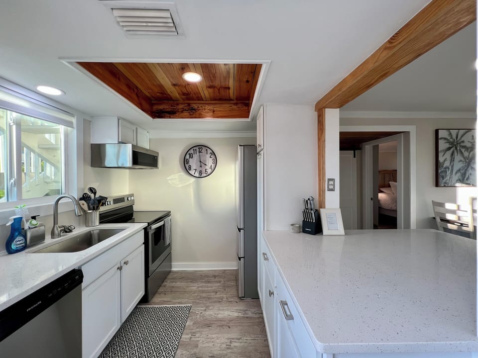 Step into your gourmet kitchen featuring gleaming white quartz counters, stainless steel appliances, and stunning wood ceiling accents that create a warm, inviting space.