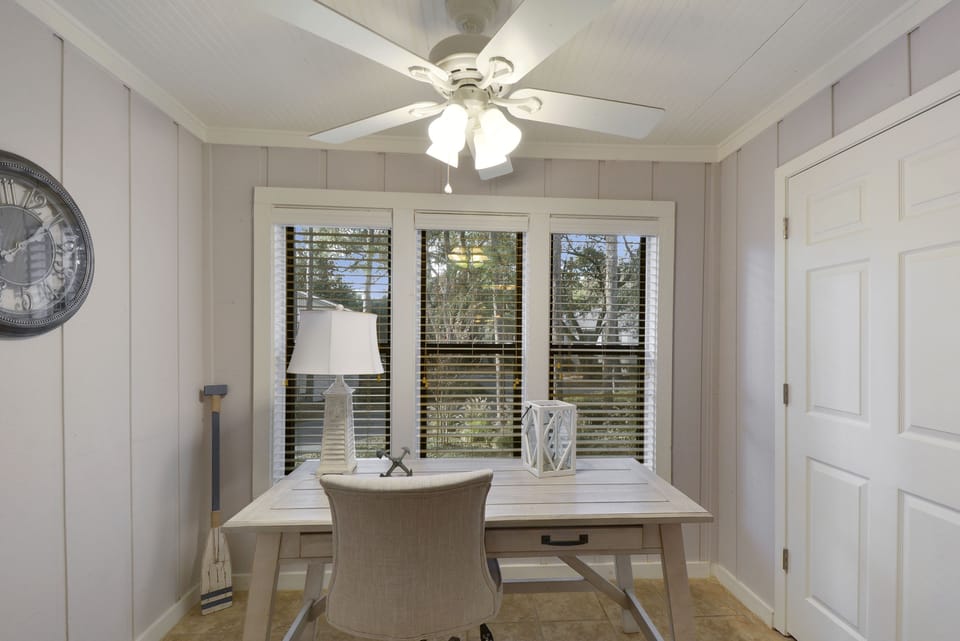 Sunroom Workspace with Desk - Window-lined sunroom with desk, chair, ceiling fan, and natural light for reading or remote work.