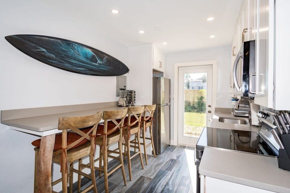 Bright kitchen with modern appliances and a surfboard wall art overlooking the backyard.