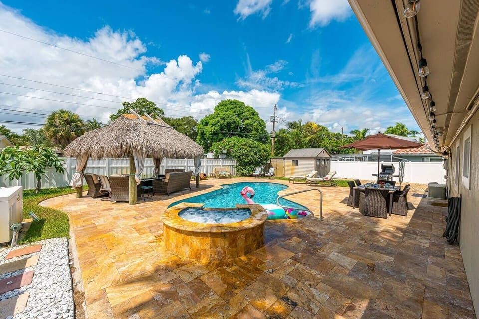A resort-style oasis in the heart of Deerfield Beach! Large heated saltwater pool with a hot tub, rustic tiki hut with a large gas-powered firepit, string lighting & smart tv. Outdoor dining table for 6 and plenty of seating and lounging for the family.