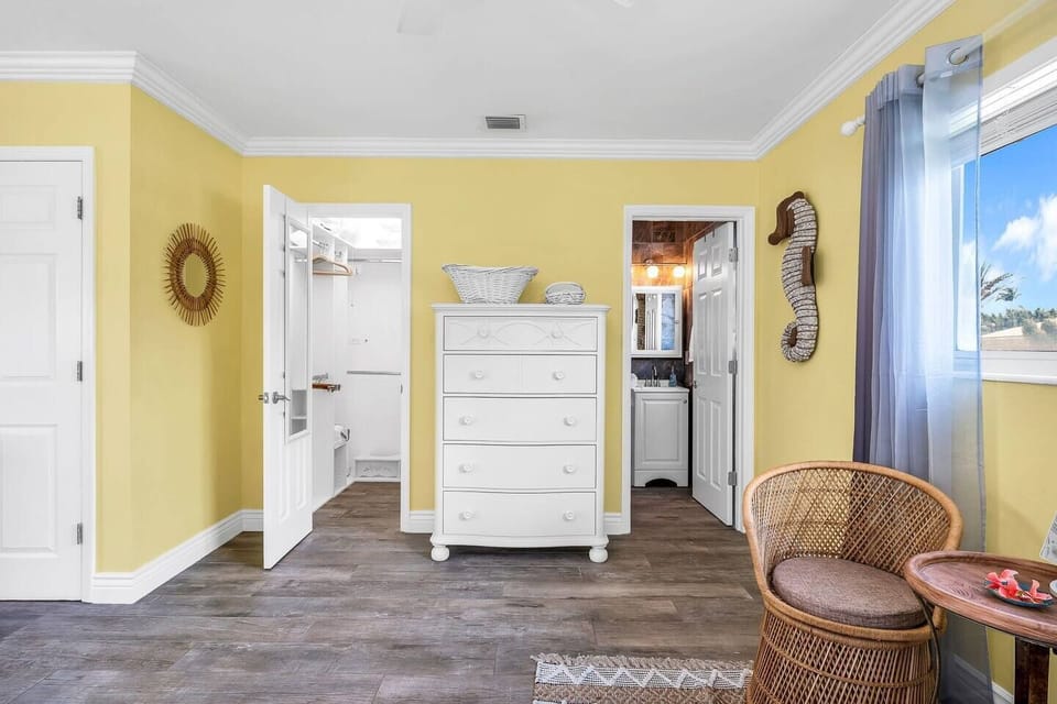Tropical-style master bedroom with sunny yellow tones, a pull-out sofa, large smart tv, and an en-suite bathroom.