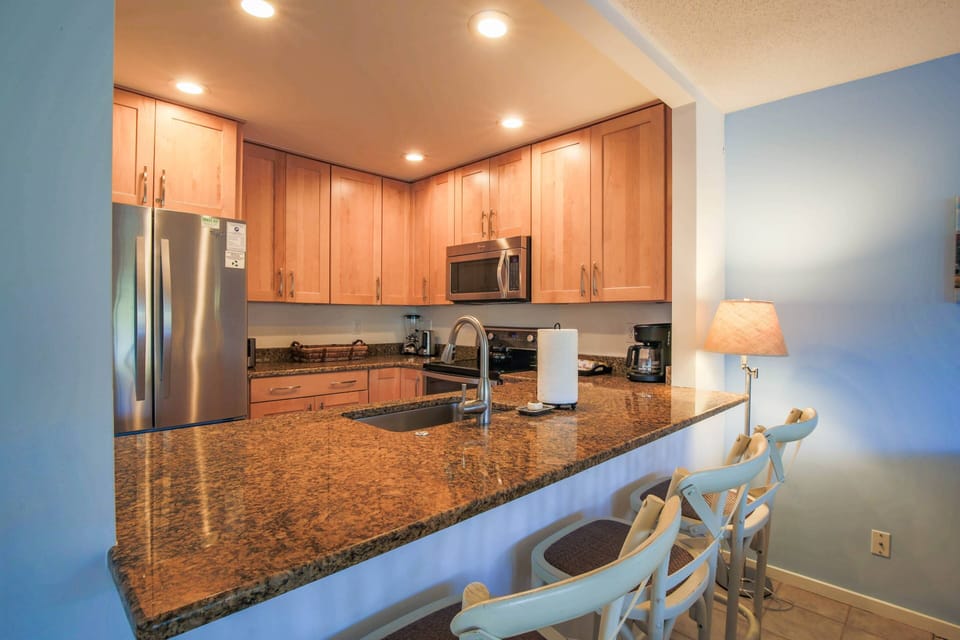 The kitchen features stainless steel appliances, granite counters and 3 stools along the counter.
