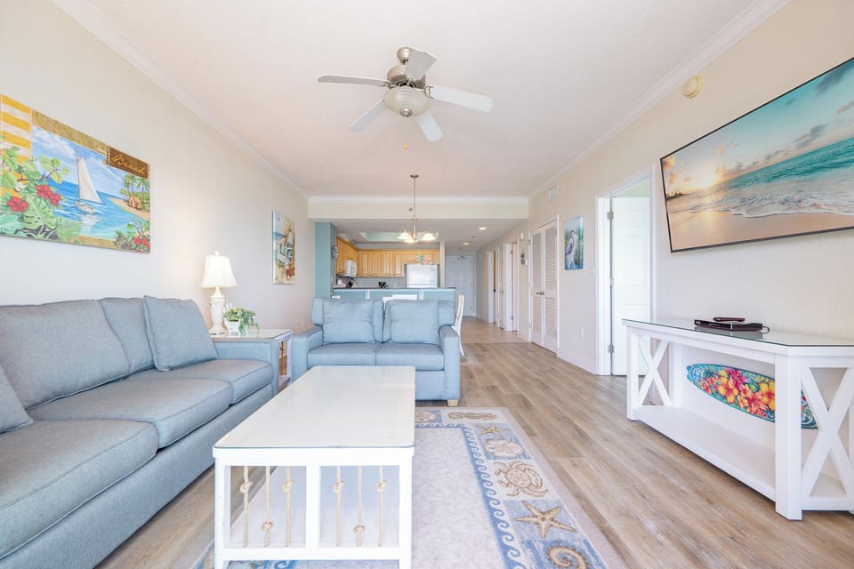 Bright and inviting living room featuring cozy blue sofas, a large TV, and beach-themed artwork for a relaxing atmosphere