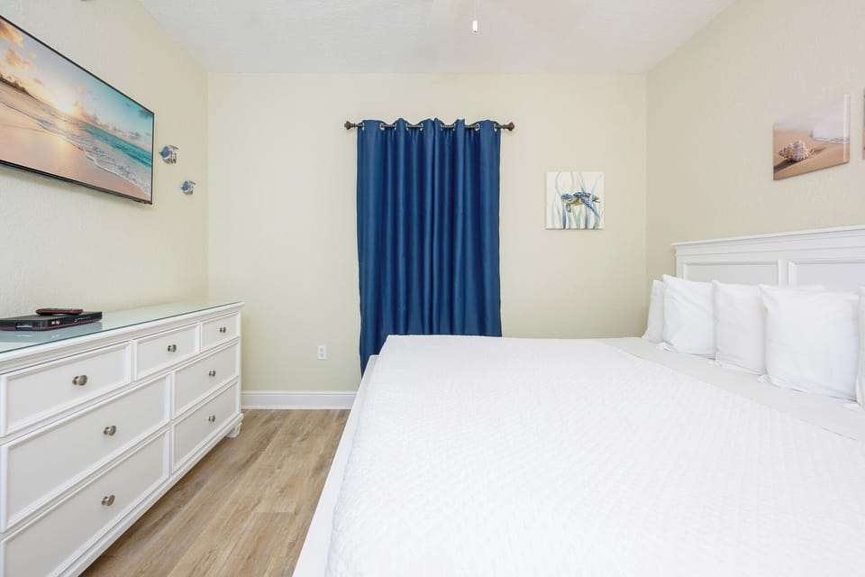 Guest bedroom featuring a large king bed, a TV, and vibrant blue curtains for a relaxing atmosphere