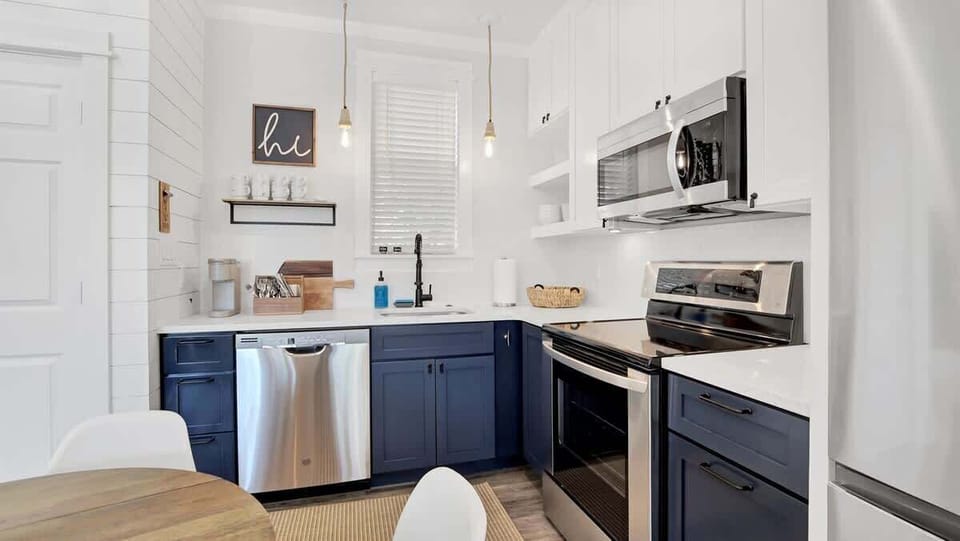 - Stylish kitchen with deep navy lower cabinets and crisp white uppers for contrast - Stainless appliances, floating shelves, and sleek quartz counters for easy prep - Pendant lights and compact layout make this space feel both modern and cozy