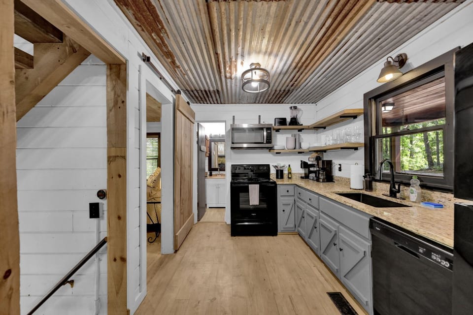 The kitchen has beautiful open shelving with plenty of dishes, glasses, & mugs.