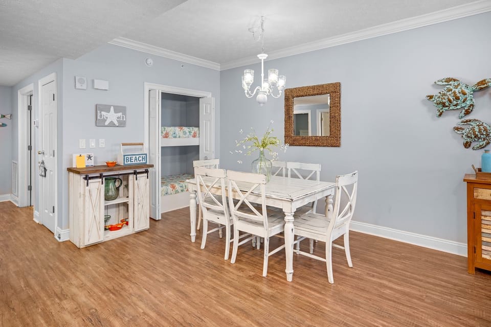 Dining area with a rustic white table and six chairs under a chandelier