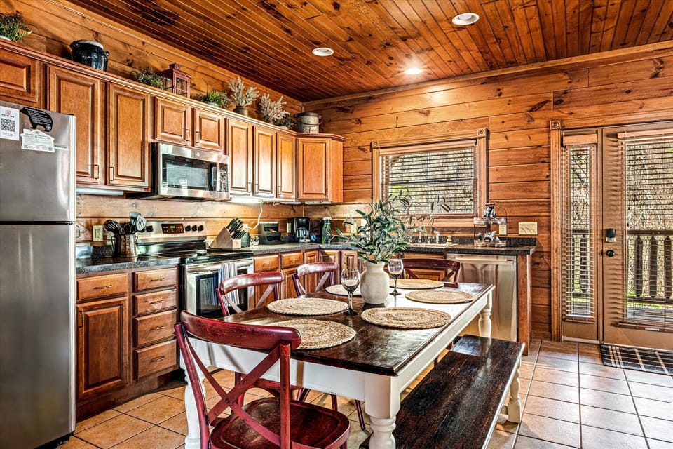 A beautiful wooden kitchen featuring stainless steel appliances, a large island with bar seating, and a cozy dining setup with red chairs.