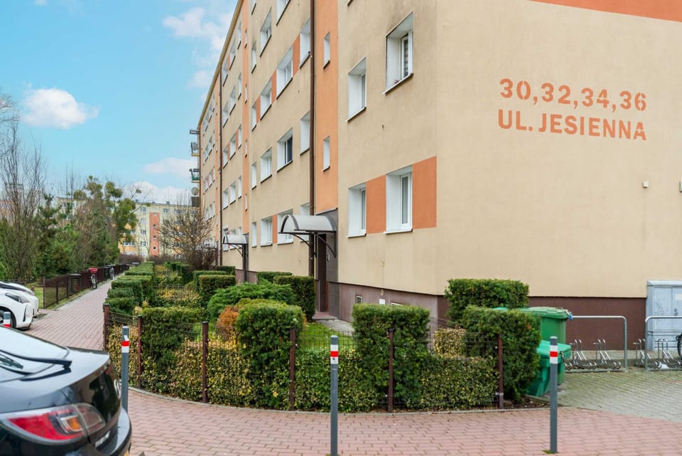 An exterior view of the residential building, showcasing its neat surroundings and parking area.

