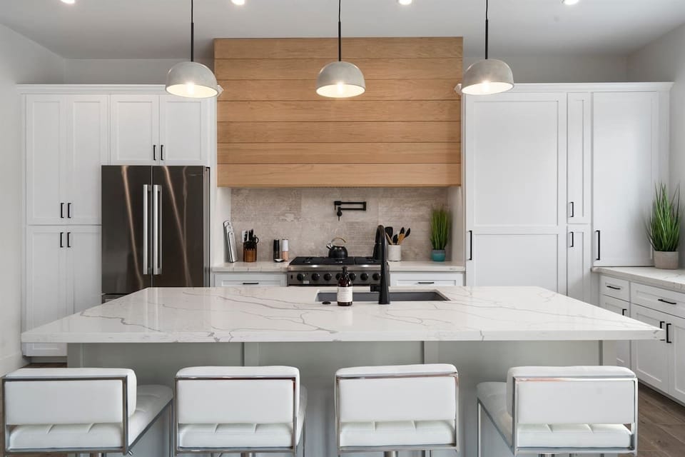 Cook in style with this full kitchen, featuring a spacious island, gas range, wine cooler, and coffee area. White decor with marble, green, and wood accents adds elegance to your culinary experience.