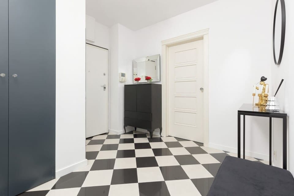 An entrance area with checkered flooring, a black cabinet, and a round mirror on the wall.
