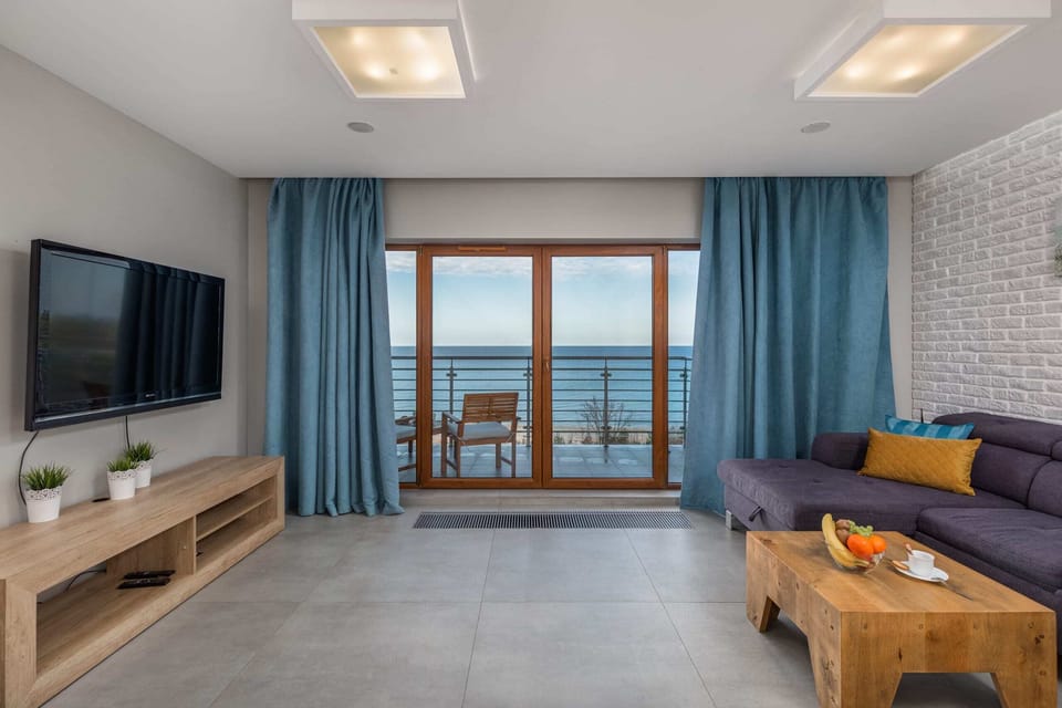 A cozy living room with a gray couch and blue curtains, featuring a wooden coffee table and a view of a balcony, letting in plenty of natural light.