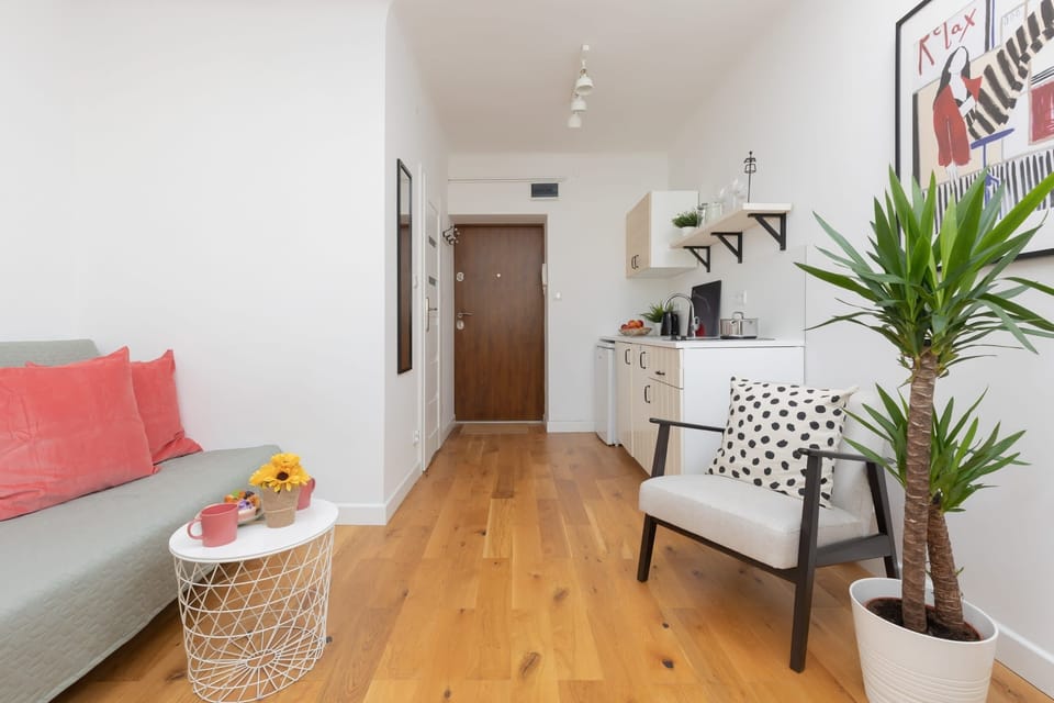 A bright hallway with a gray sofa, wooden floor, and houseplants creating a welcoming ambiance.
