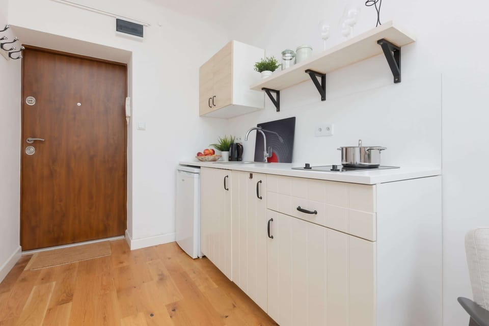 A kitchen view featuring white cabinetry, open shelves, and a wooden door adding warmth.
