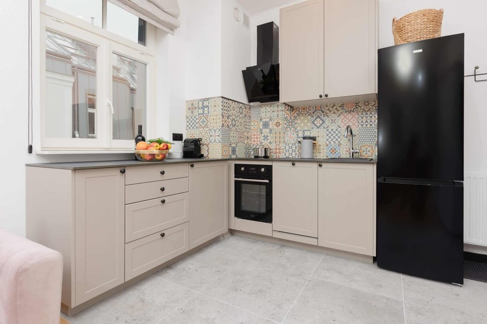 A modern kitchen with beige cabinets, a black fridge, and patterned backsplash tiles.
