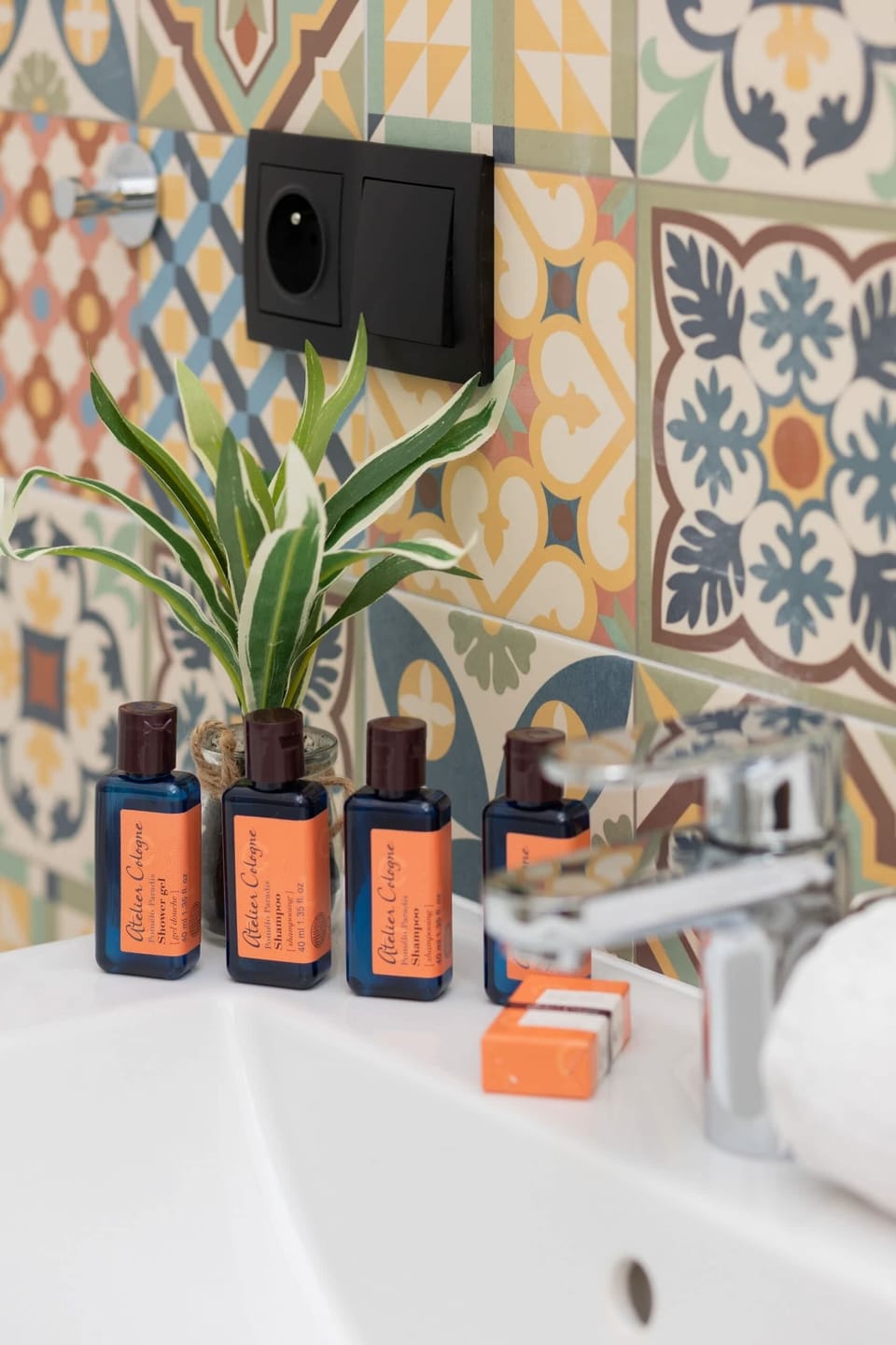A close-up of complimentary toiletries arranged with vibrant patterned tiles and plants for a welcoming atmosphere.
